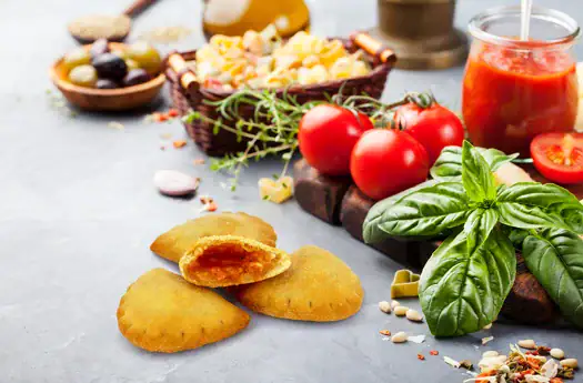 Knusprige Teigtaschen mit Tomaten, Basilikum und Tomatensauce auf grauem Hintergrund.
