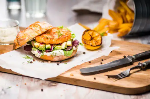 Knuspriges Fischburger mit frischem Gemüse und Zitronenspalte auf Holzbrett.