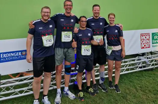 Hochleistungsteam bei einem Laufwettbewerb, alle in VALIO-Teamshirts, vor grünem Hintergrund.