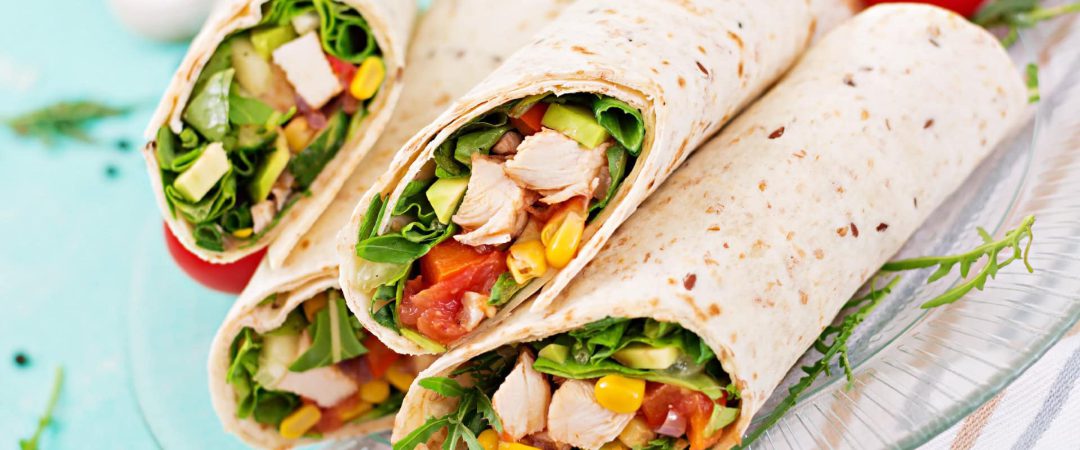 Frischer Hähnchen-Tortilla mit Salat und Gemüse, auf einem weißen Teller serviert.